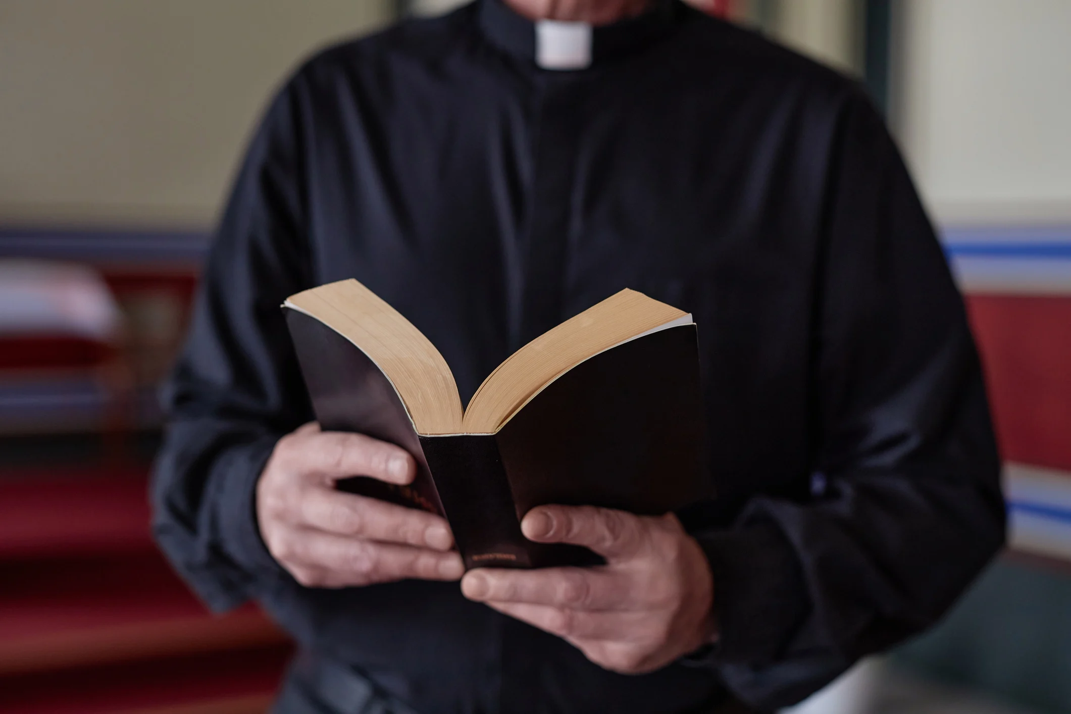 Person dressed in clerical attire holding an open book indoors.