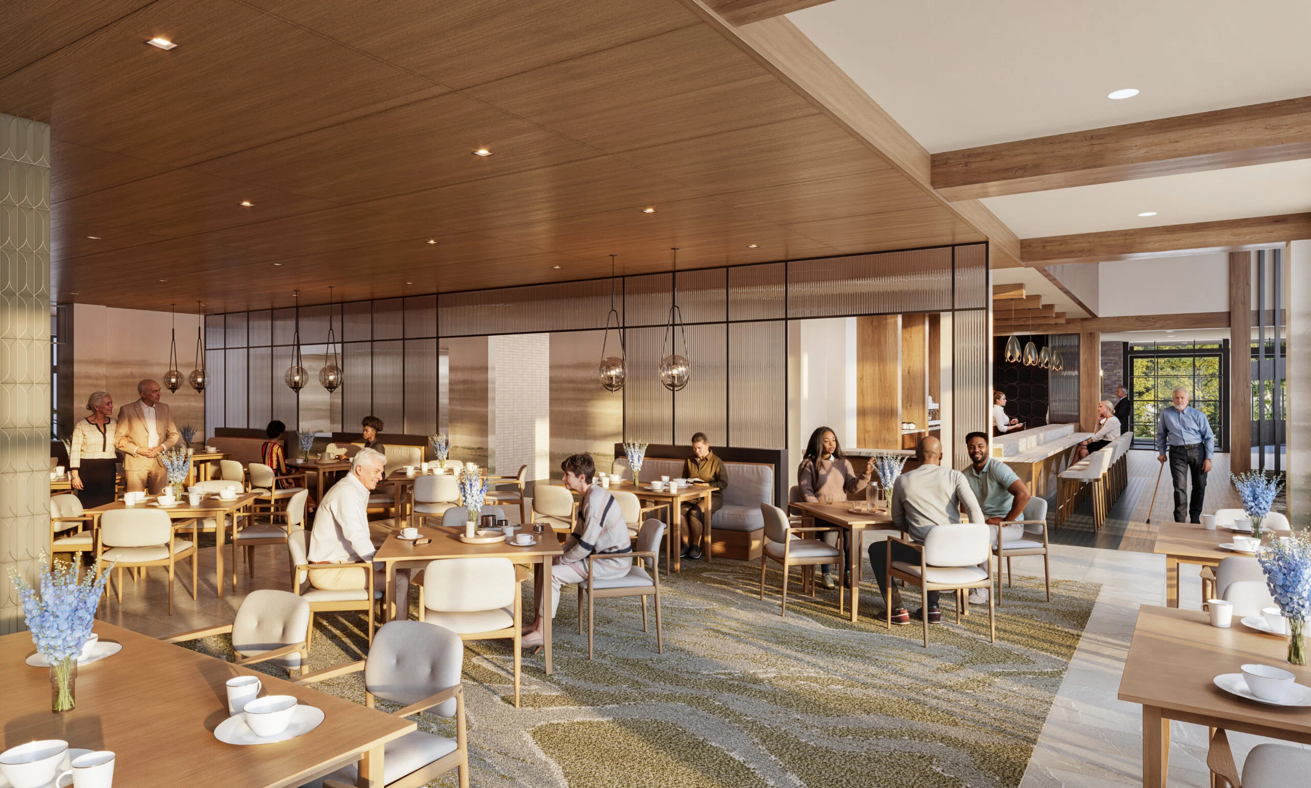 Residents dining and socializing in a spacious, sunlit community dining room with wooden furniture and decorative flowers on tables.