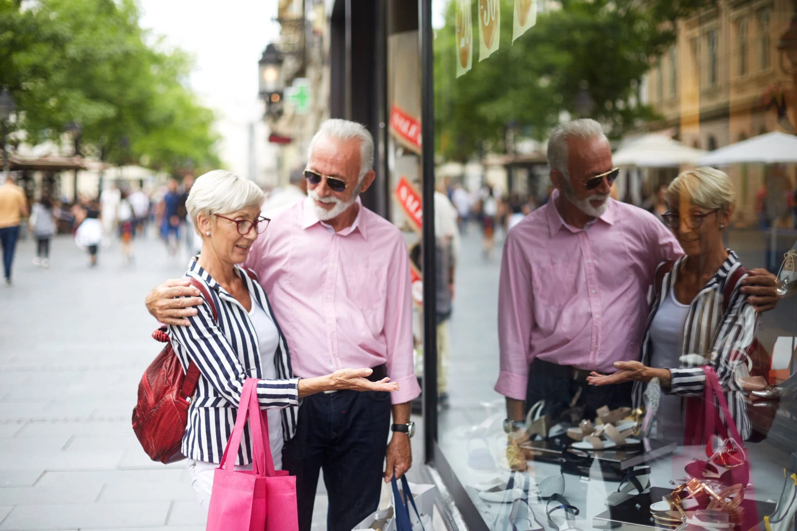 Older couple standing together on a city street looking at shoes in a store window, enjoying a moment of social engagement.