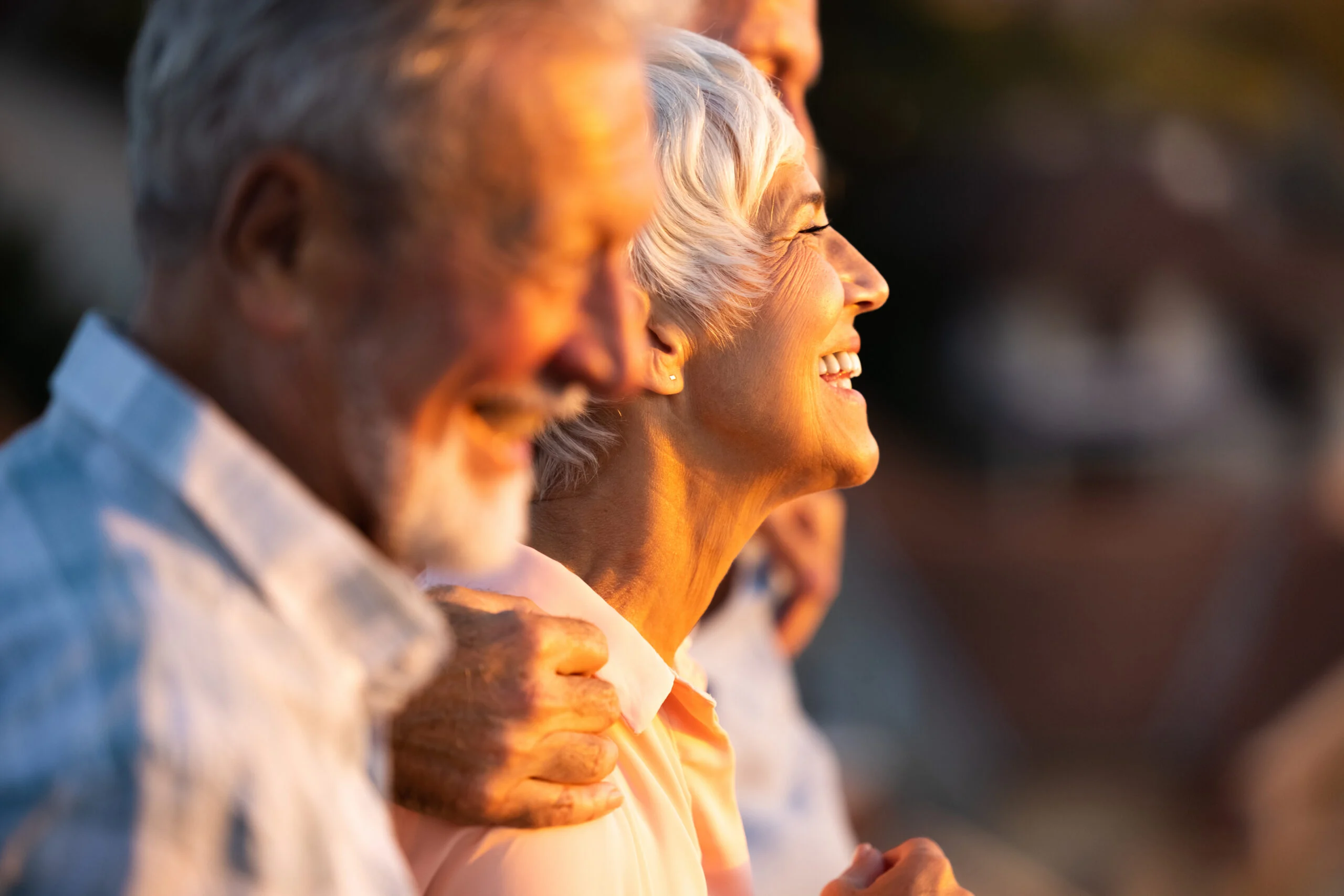 Two seniors smiling and enjoying a peaceful outdoor social moment together at sunset.