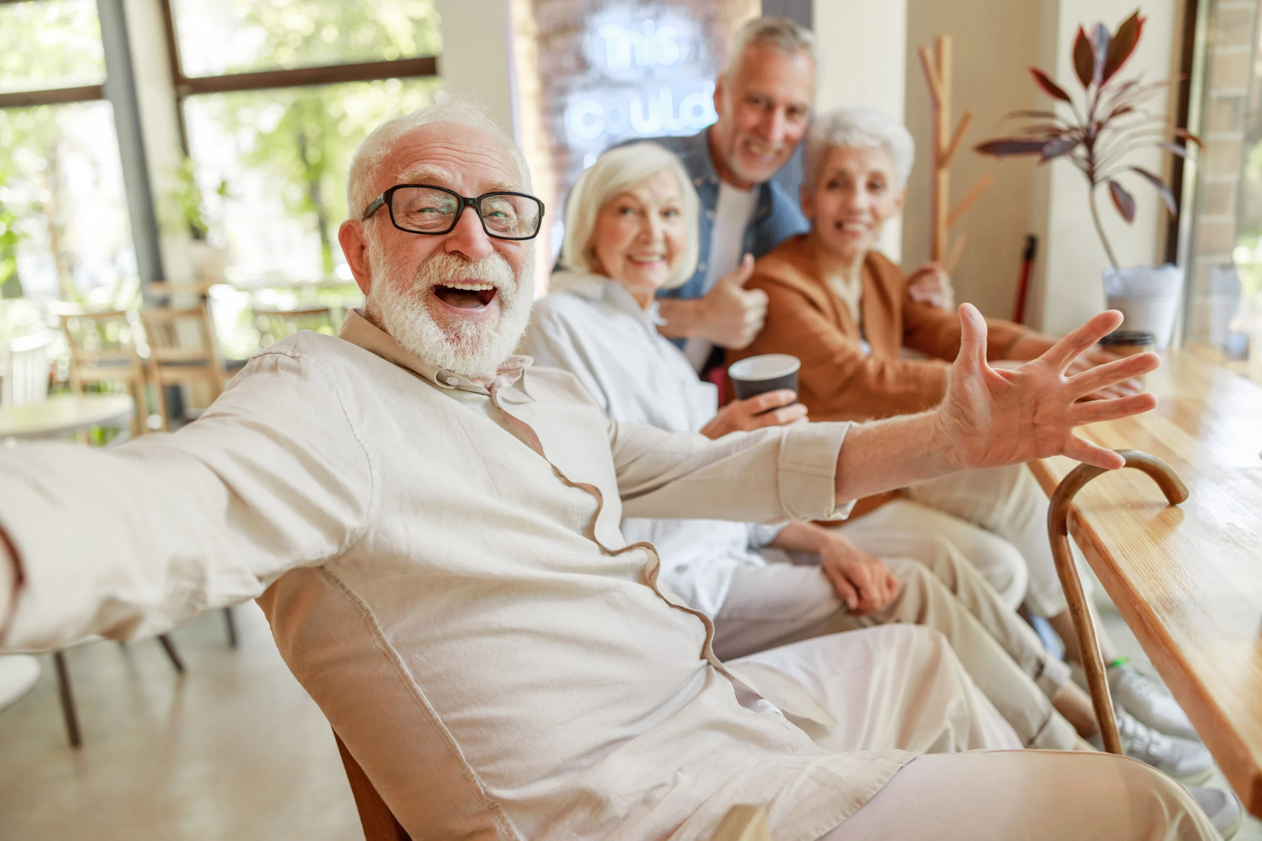 Four seniors smiling and socializing while seated at a wooden counter with beverages in a bright community space.