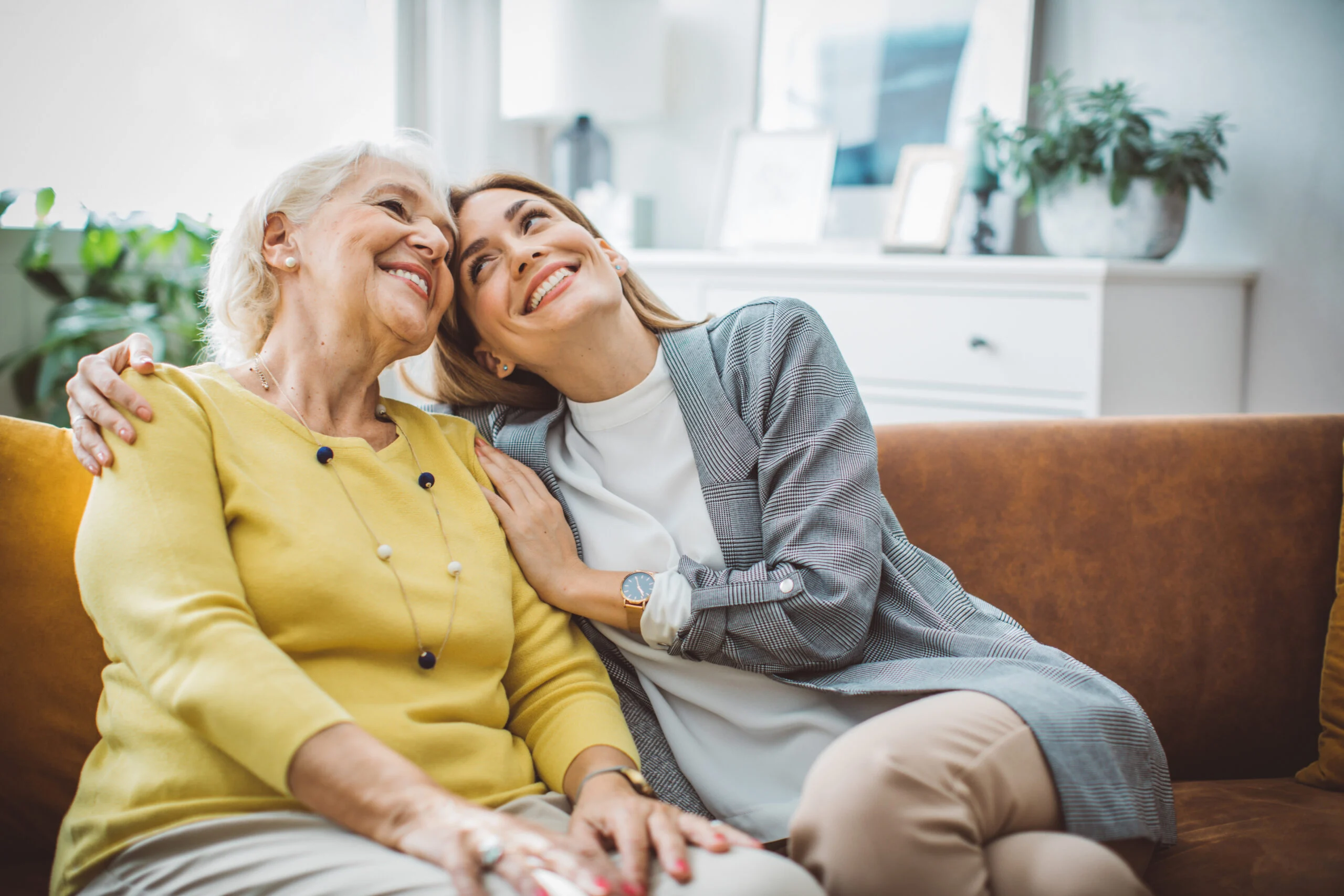 Two women sitting together on a couch sharing a warm, affectionate moment in a senior living community room.
